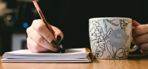 Writing website copy that converts with a positive mindset – hand with pen and “Be Happy” mug
